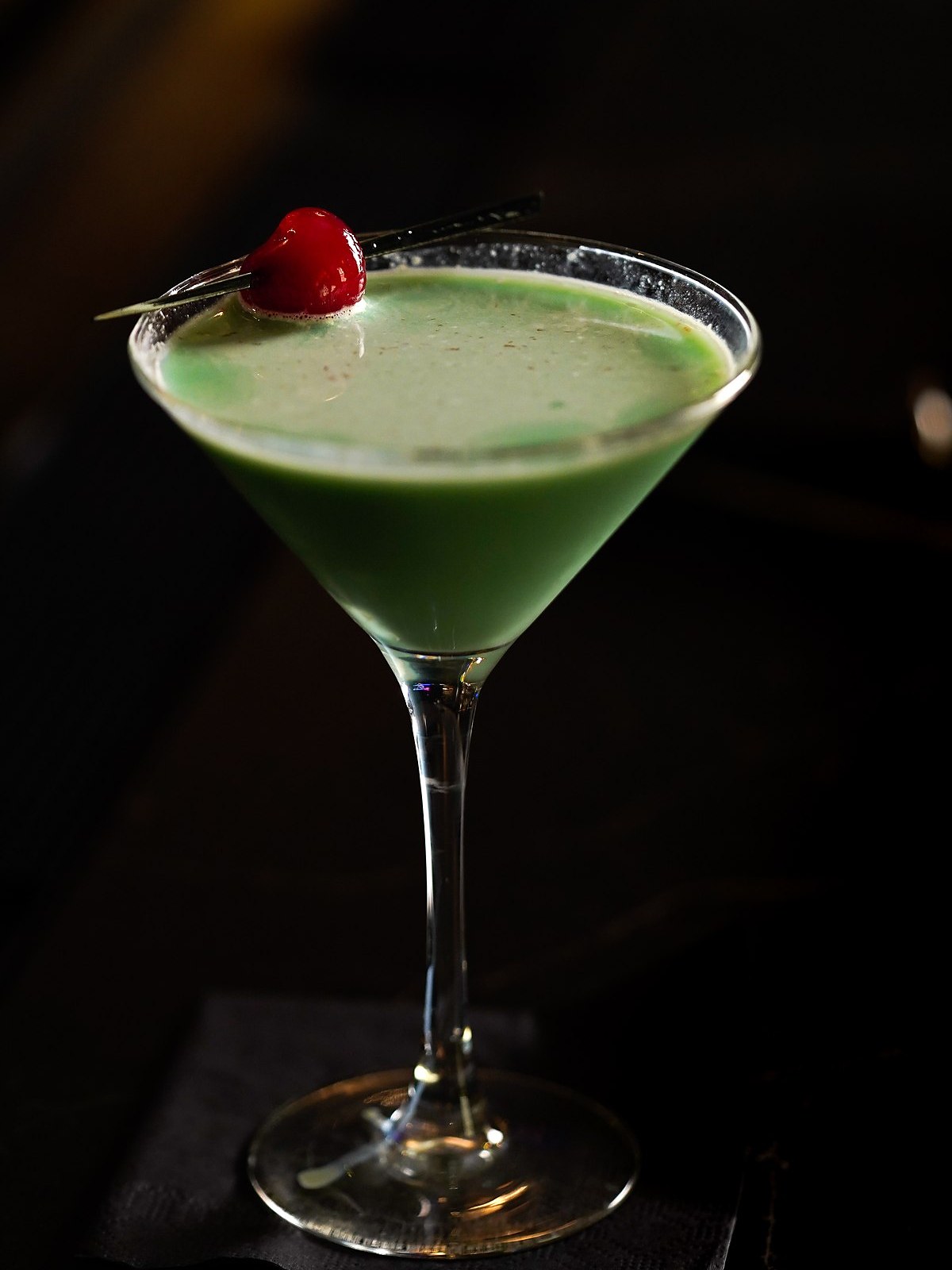 A pale green cocktail served up, with a cherry, on the bar at OldeStone