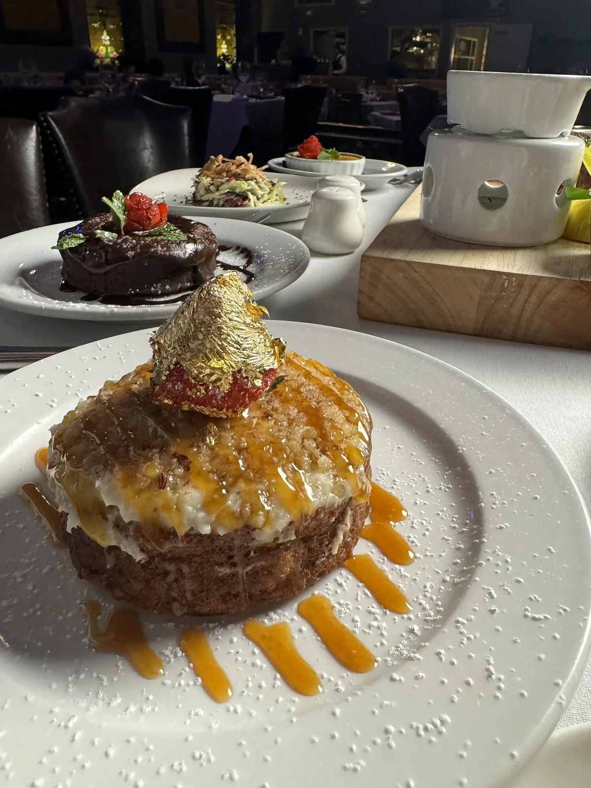 A dessert finished with caramel and gold leaf, the dining room behind