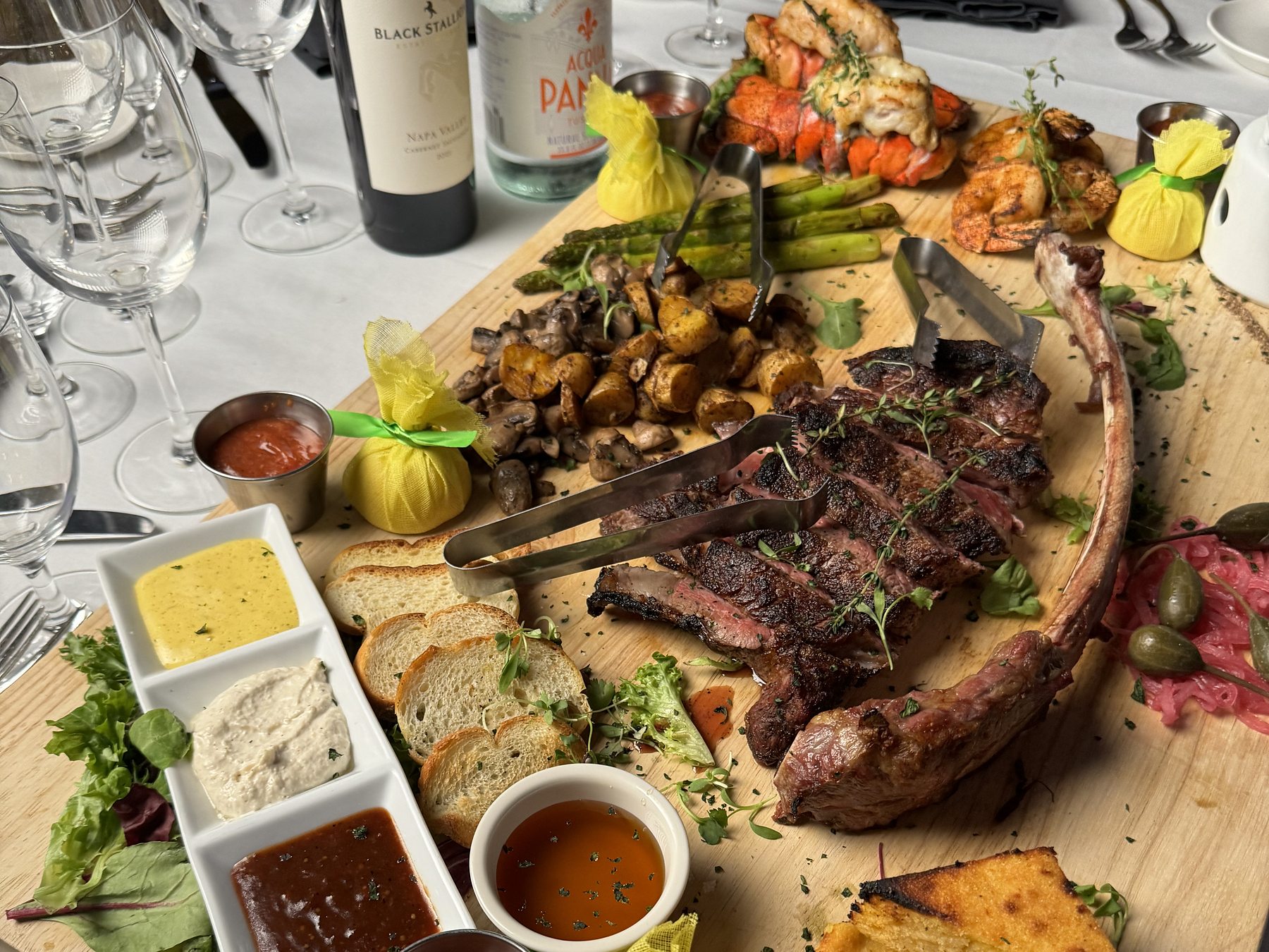 The surf and turf board: a tomahawk sliced on a wooden plank with lobster tail, shrimp, roasted potatoes, cornbread and a row of sauces