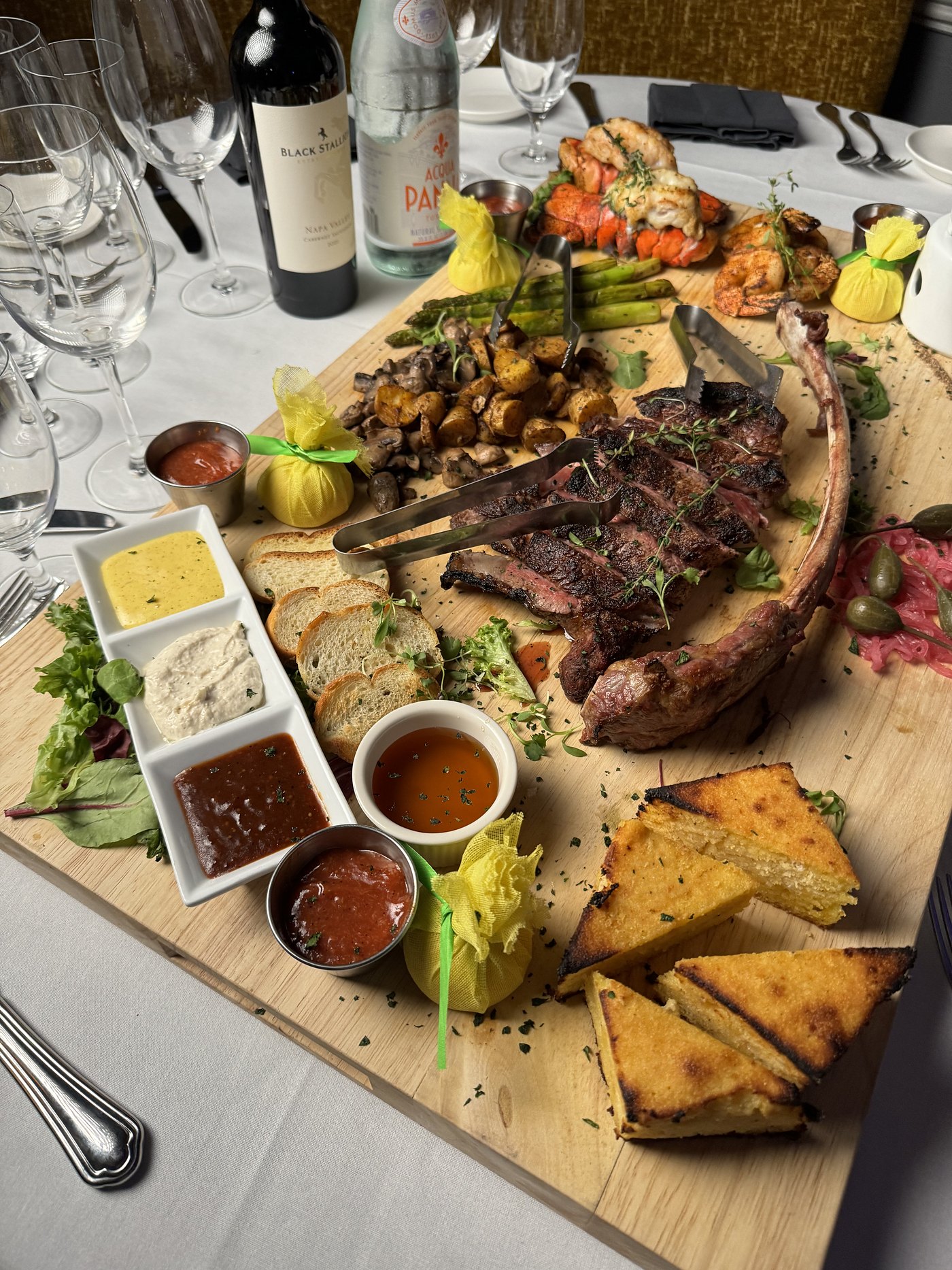 The surf and turf board: a tomahawk sliced on a wooden plank with lobster tail, shrimp, grilled asparagus, roasted potatoes, mushrooms, cornbread and a row of sauces