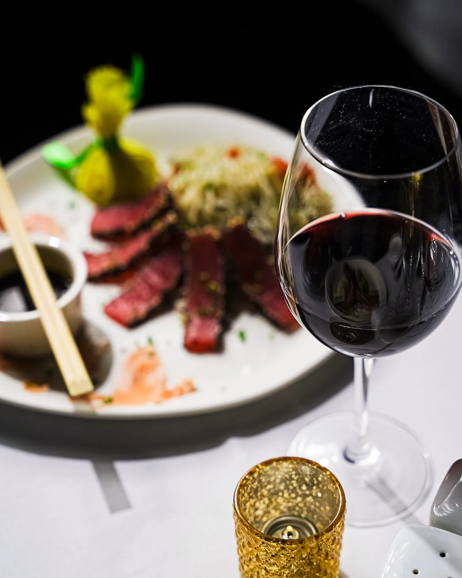 Sesame crusted seared tuna with noodles, beside a glass of red wine