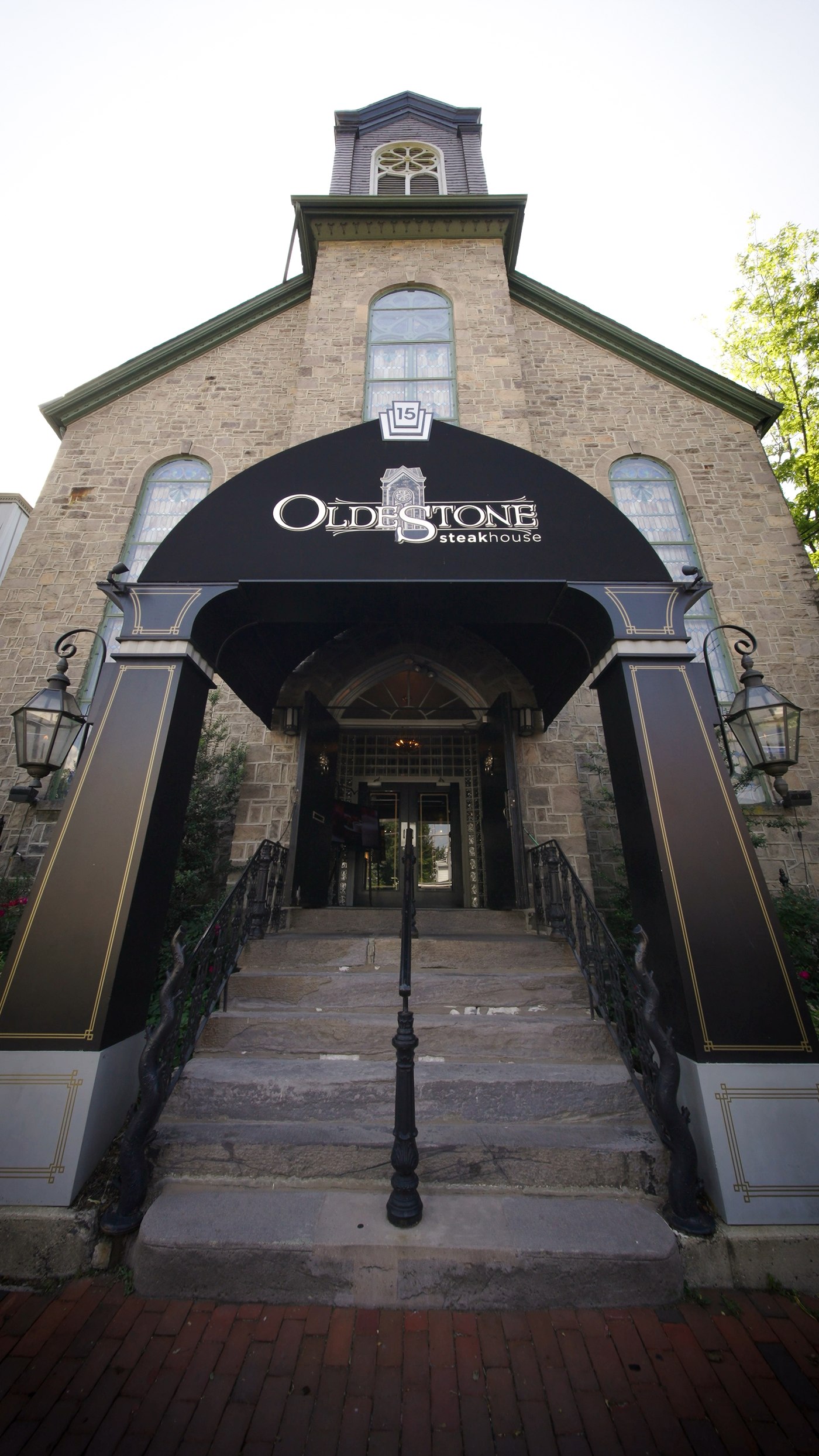 The stone front of OldeStone Steakhouse on South Main Street, with its black awning, gas lanterns and the steps up to the entrance